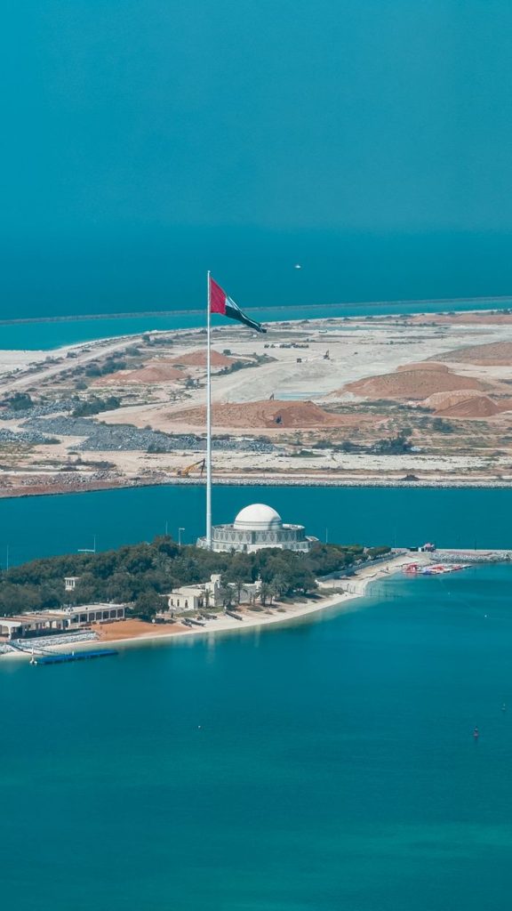 Aerial view of the UAE flag on Corniche Abu Dhabi with coastal landscape.